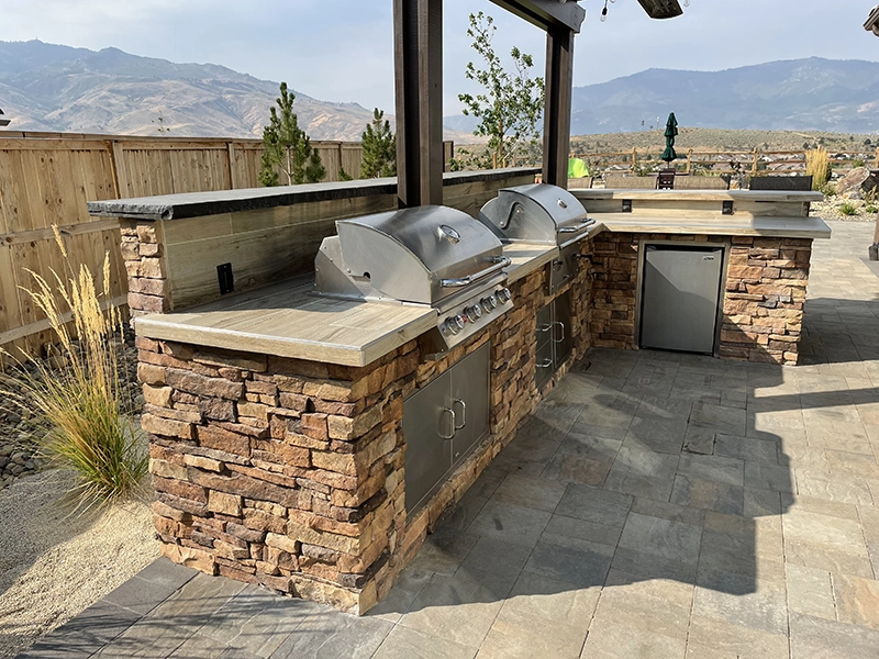 A custom outdoor kitchen area with a wall with grills and a mini-fridge built in.