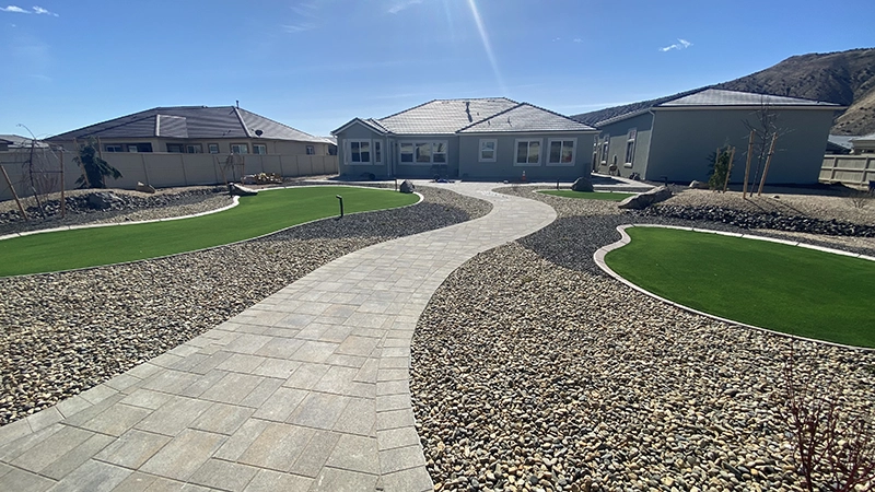 Professional landscaping of a concrete brick walkway and small stone beds with putting greens on either side.