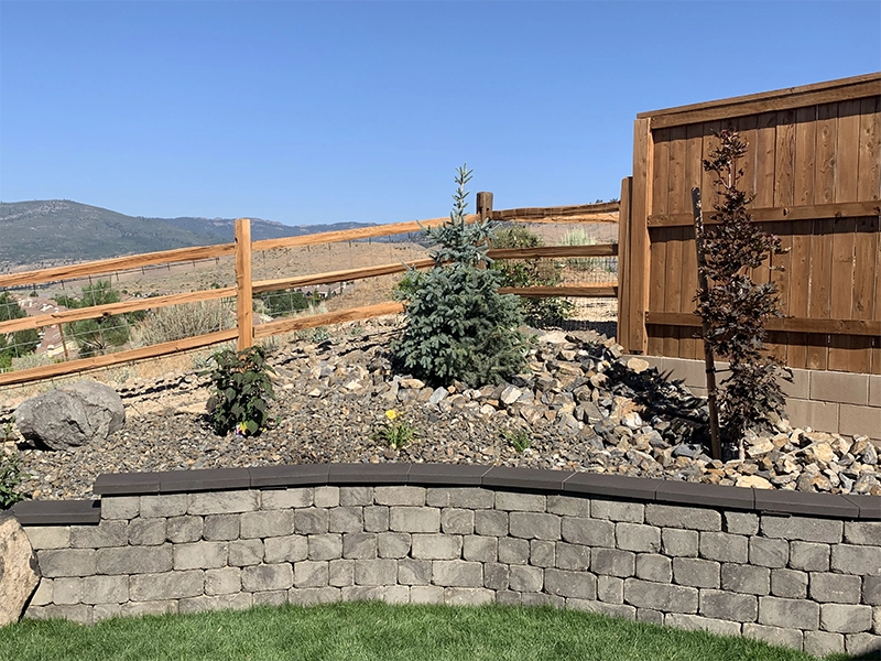 A retaining wall with a rock bed, bushes, and a wooden fence above.